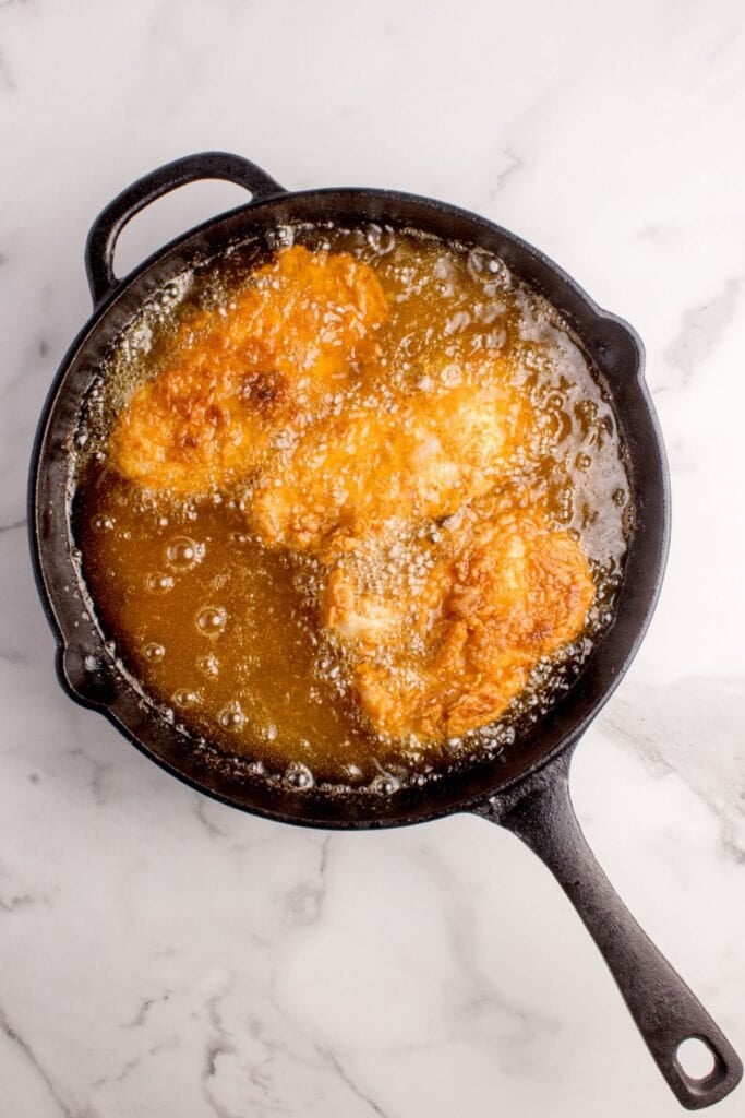 Buffalo chicken being fried in a cast iron pan.