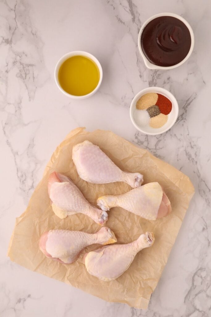 Raw chicken drumsticks on parchment paper.