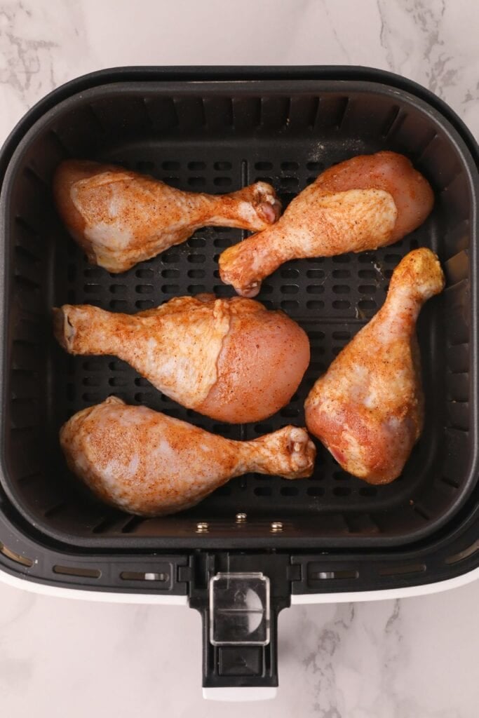 Raw chicken drumsticks in an air fryer basket.