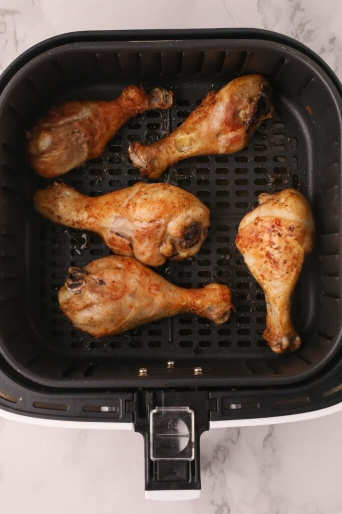 Cooked drumsticks in an air fryer basket ready to be basted with BBQ sauce.
