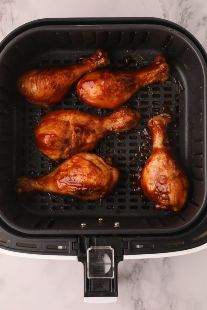 Cooked chicken drumsticks in the air fryer with BBQ sauce on top.