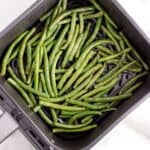 Raw fresh green beans in the air fryer basket about to be air fried.