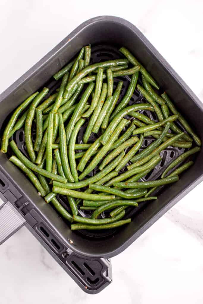 Raw fresh green beans in the air fryer basket about to be air fried.