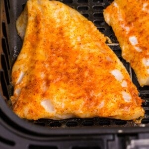 Cooked cod in an air fryer basket.