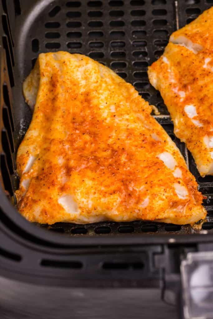 Cooked cod in an air fryer basket.