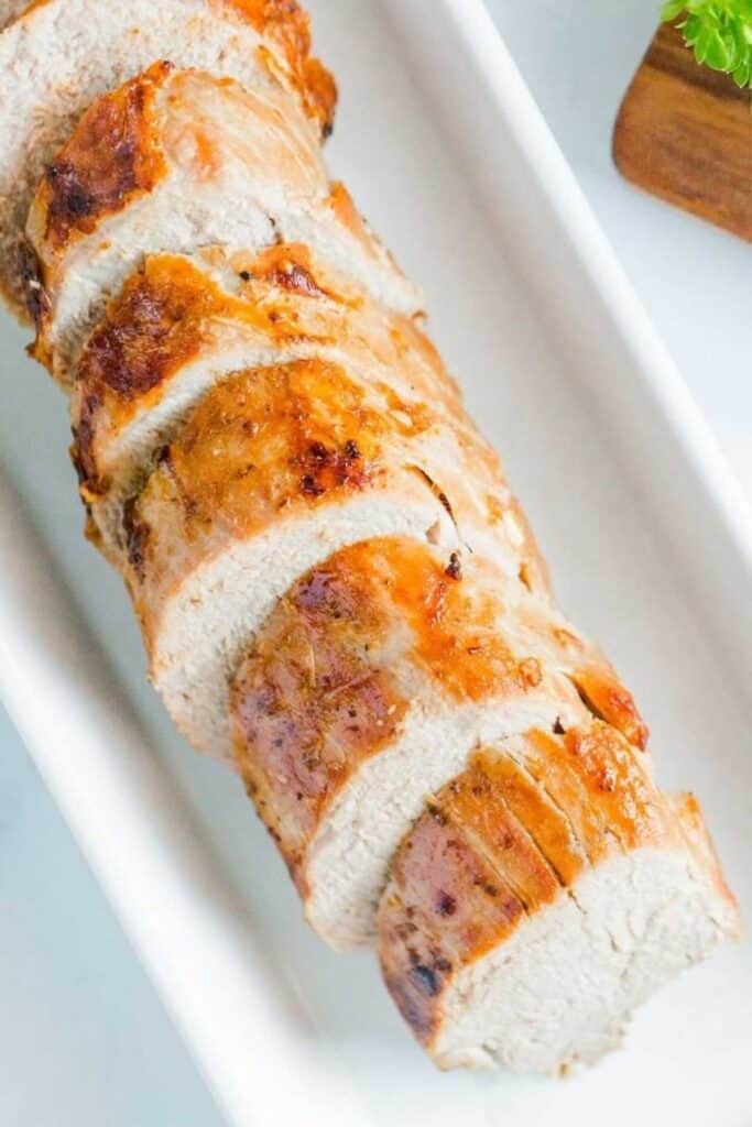 Close up of air fryer pork tenderloin cut into medallion pieces on a white serving platter.