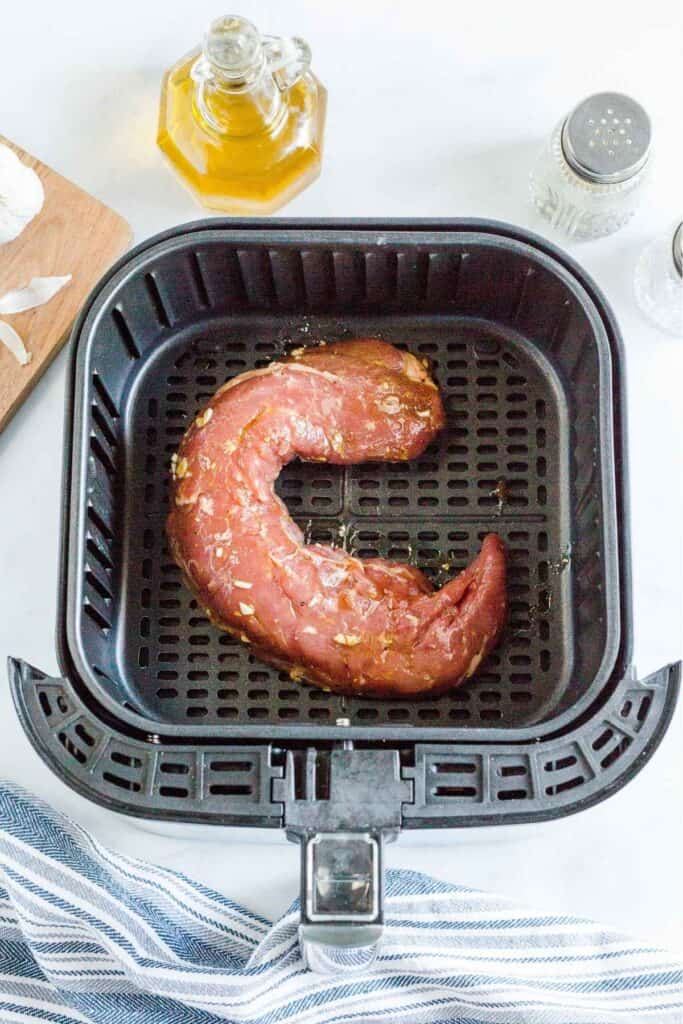 Raw pork tenderloin in an air fryer basket about to be cooked.