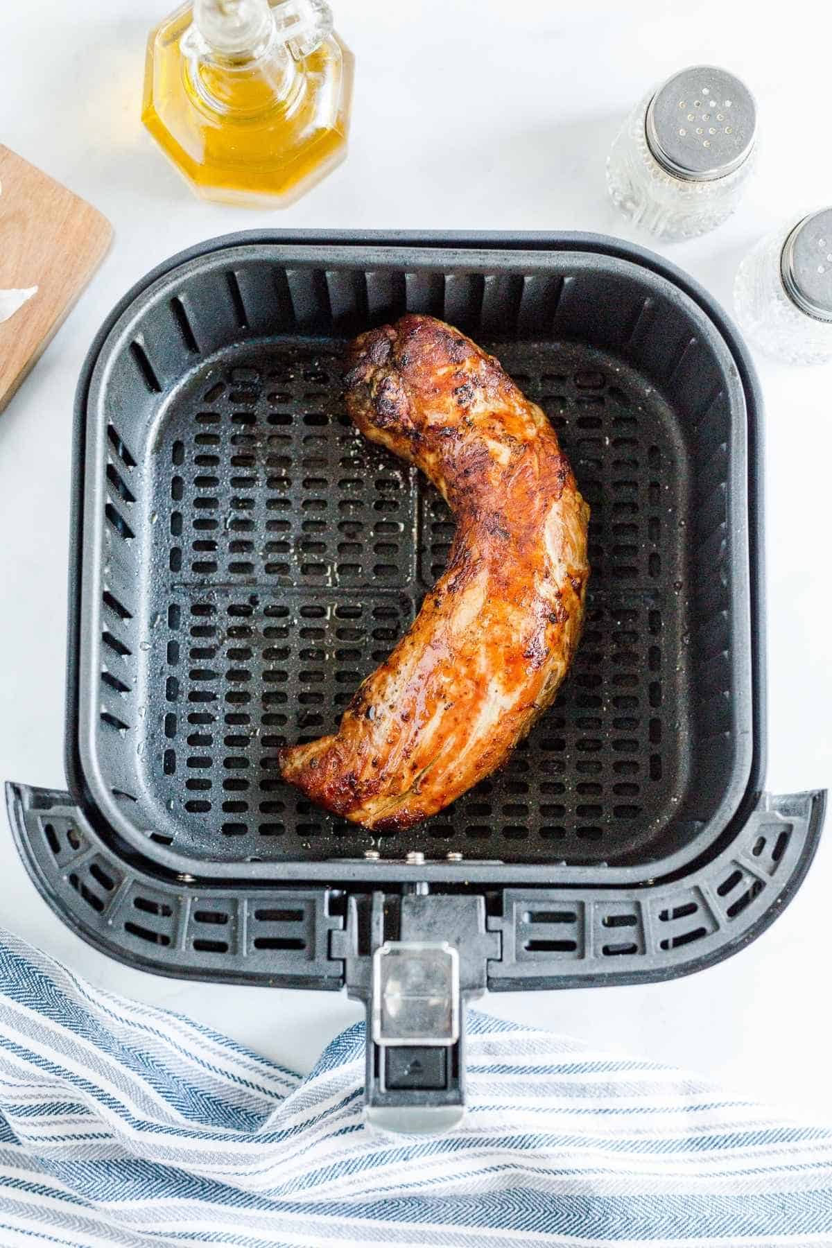 Cooked pork tenderloin in an air fryer basket.