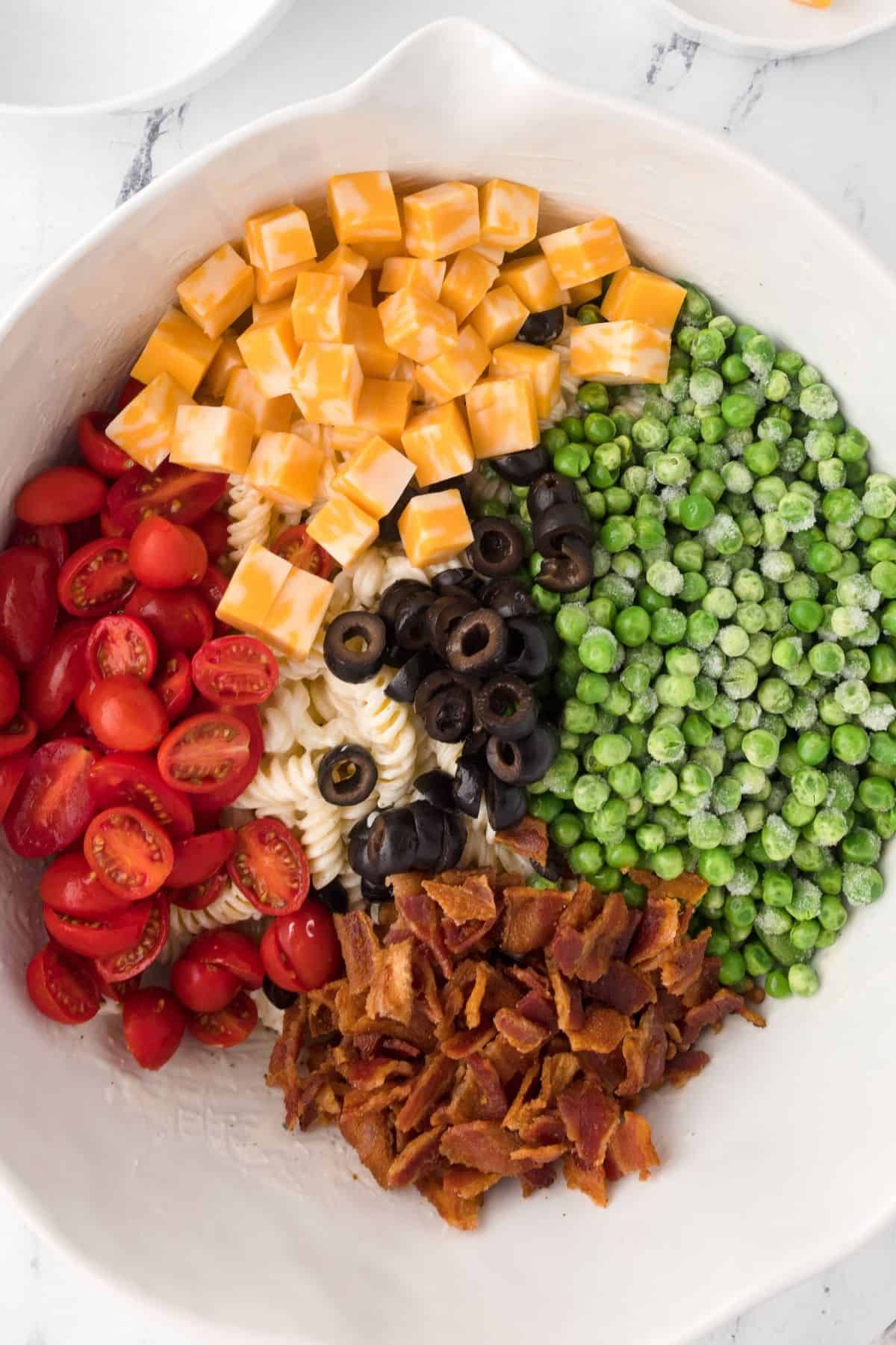 Vegetables and toppings being added to the pasta salad bowl.