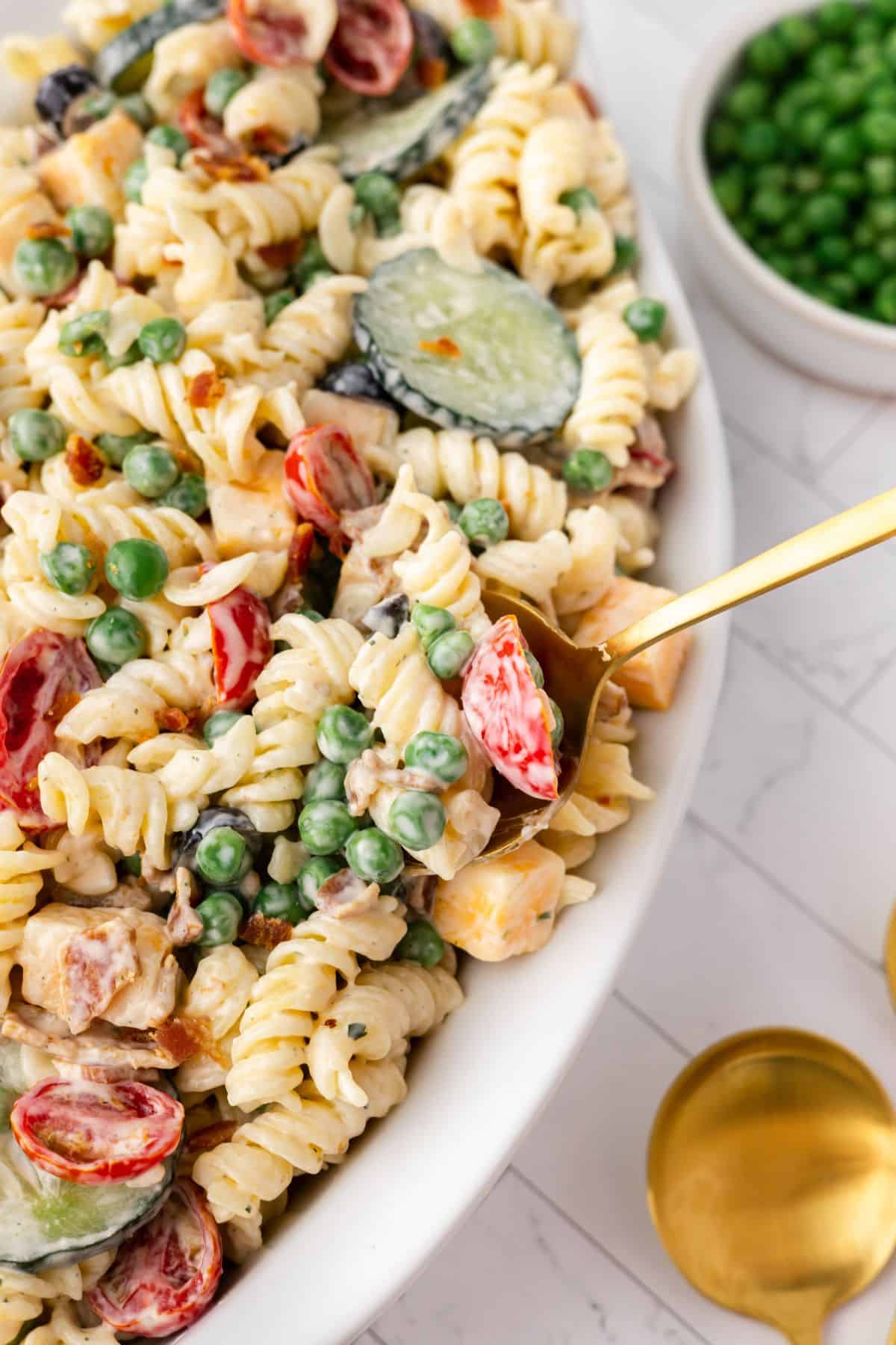 View of the bacon ranch pasta salad in the serving dish with a spoon in it.