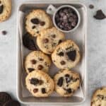 Oreo cheesecake cookies in a small tin storage dish with a side of chocolate chips.