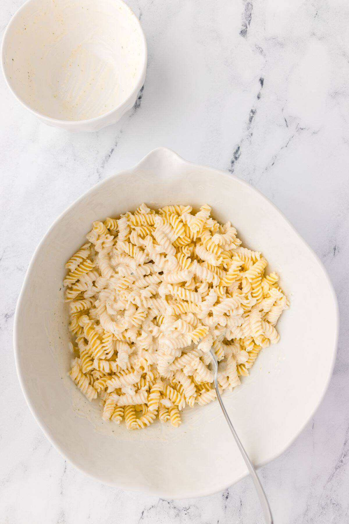 Pasta salad dressing being mixed into the rotini pasta.