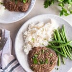 Overhead view of Cube Steak with rice and green beans on a white plate.