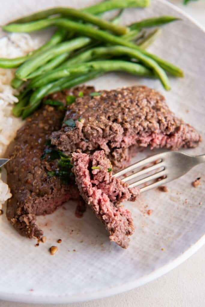 Slice of cube steak with rice and green beans on a white plate.