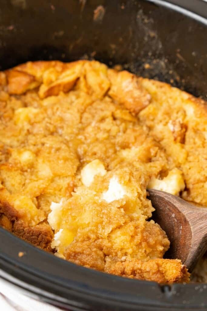 overhead view of a wooden spoon scooping out a serving of crockpot french toast casserole.