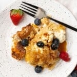 Overhead view of Crockpot French Toast Casserole on a white plate with berries and a fork.