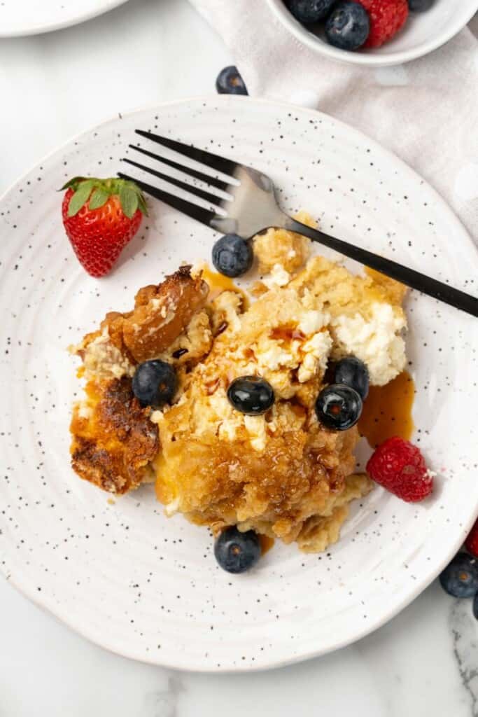 Overhead view of Crockpot French Toast Casserole on a white plate with berries and a fork.