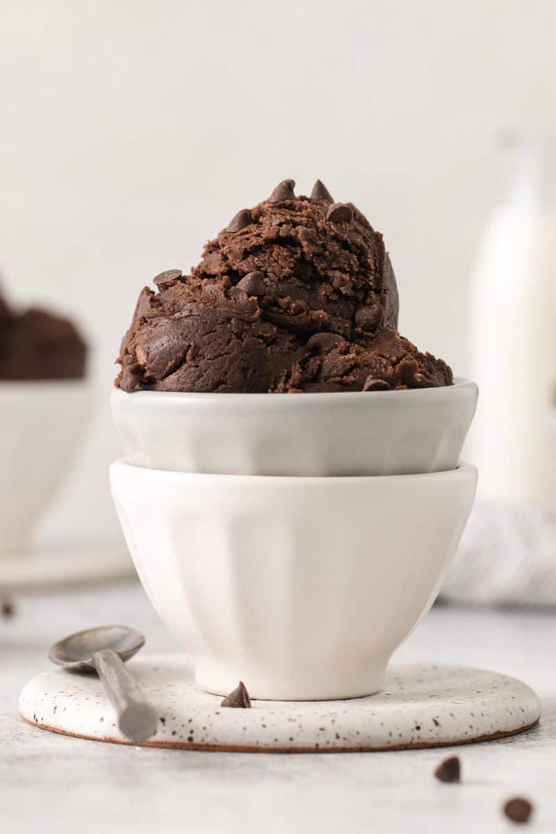 Scoops of edible brownie batter in a stack of white bowls resting on a saucer.