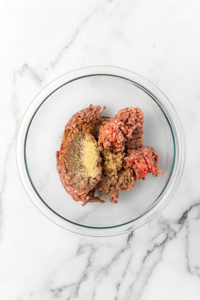 Combining ingredients to prepare Ninja Foodi Hamburgers in a clear mixing bowl.