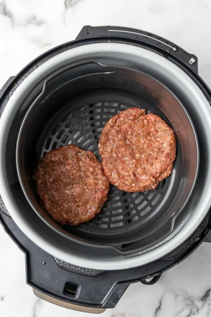 2 hamburger patties resting in the bottom of a Ninja Foodi ready to be cooked.