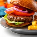 Prepared Ninja Foodi Hamburger with lettuce, tomato, pickles, and onions on a gray plate.