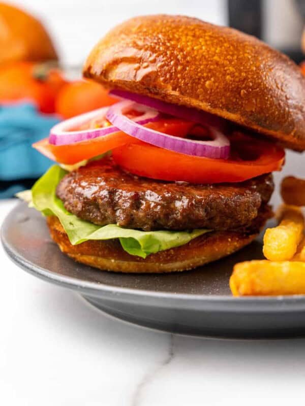 Prepared Ninja Foodi Hamburger with lettuce, tomato, pickles, and onions on a gray plate.