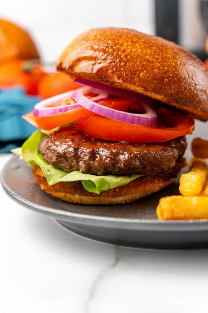 Prepared Ninja Foodi Hamburger with lettuce, tomato, pickles, and onions on a gray plate.