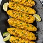 Plated cajun corn on the cob recipe on a black serving dish with lime wedges.