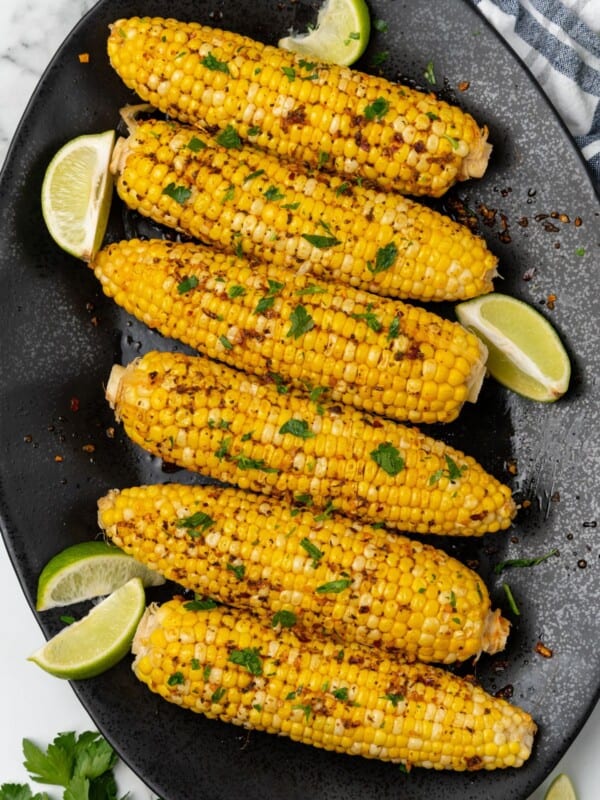 Plated cajun corn on the cob recipe on a black serving dish with lime wedges.