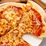 Lifting a slice of air fryer tortilla pizza off a white plate.