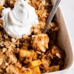 Spoon scooping a bite of prepared air fryer apple crisp in a white baking dish.