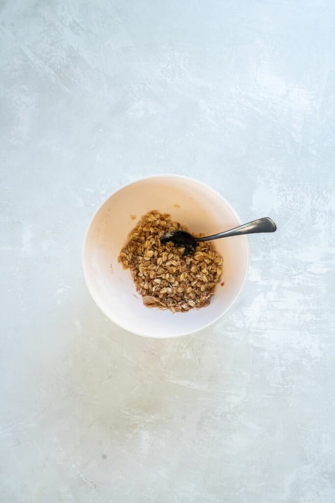 Topping ingredients for apple crisp combined in a white bowl with a spoon.