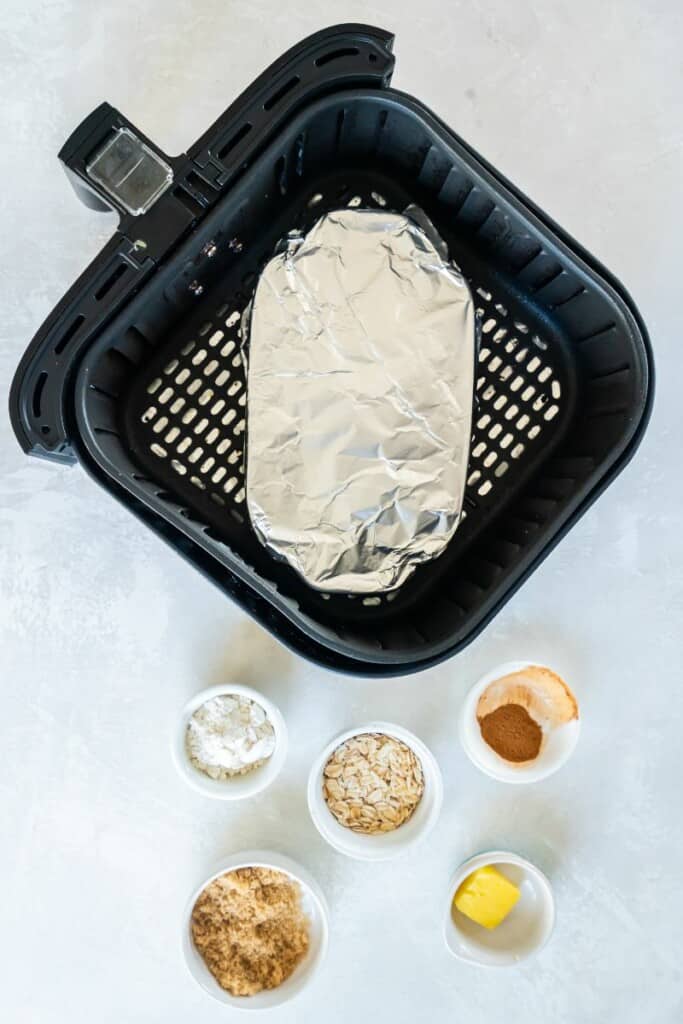 Apple Crisp dish in a black air fryer basket covered in foil.