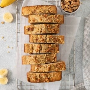 Loaf of banana bread cut into slices on a cooling rack.