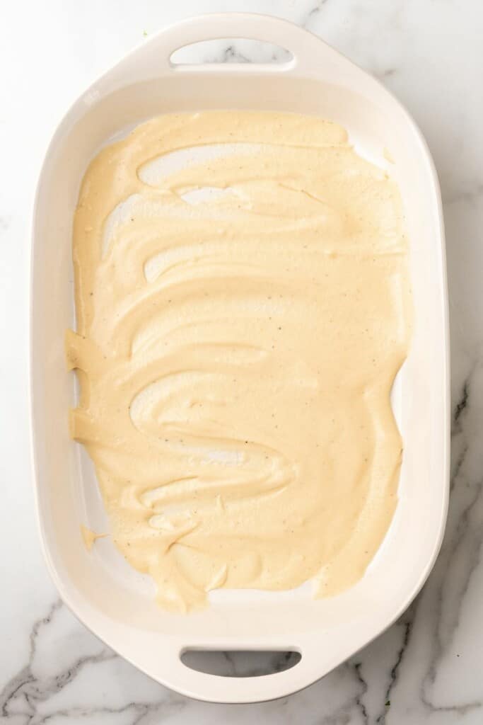 Alfredo sauce spread across the bottom of a 9x13 casserole dish.