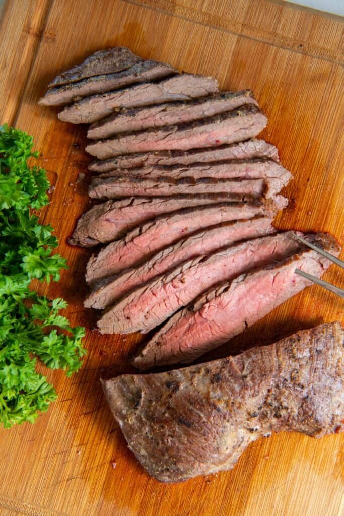 Slicing a flank steak on a wooden cutting board.
