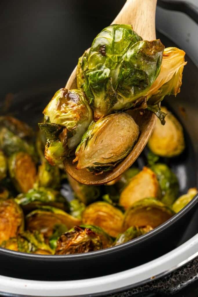 Wooden spoon holding a bite of brussels sprouts resting in a ninja foodi.