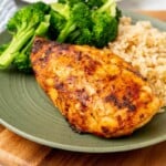 A chicken breast with broccoli and rice on a green plate.