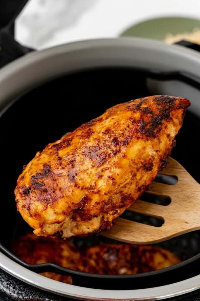 Close up view of a seasoned chicken breast being lifted out of a Ninja Foodi.