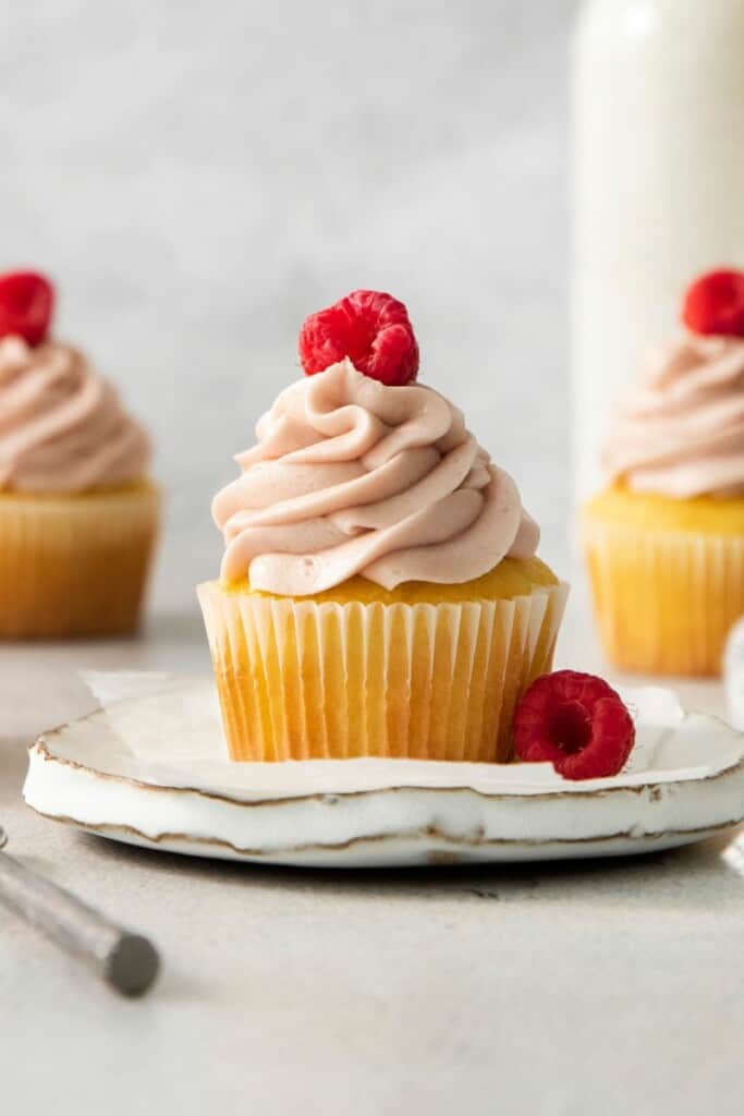 A cupcake topped with raspberry cream cheese frosting and fresh raspberries.