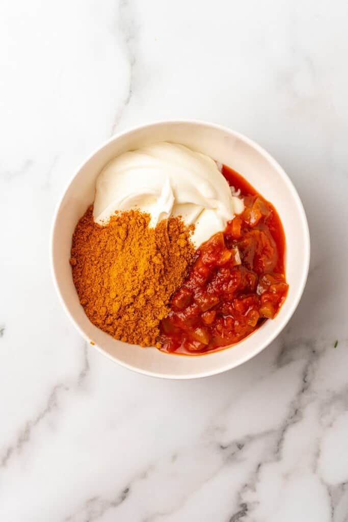 Overhead view of taco seasoning, salsa and sour cream in an offwhite bowl.