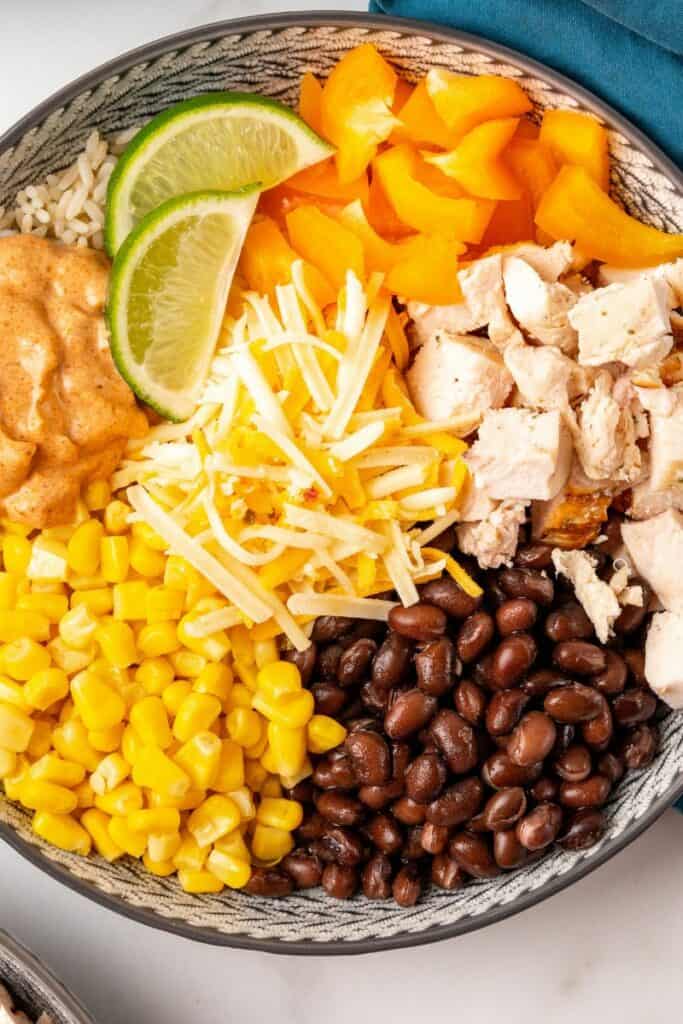 Each ingredient for southwest bowls on top of rice in a gray bowl, ready to be stirred together.