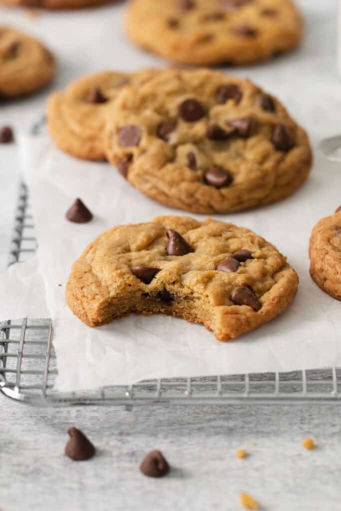 No butter cookies with chocolate chips on a wire rack with one cookie with a bite taken out of it.