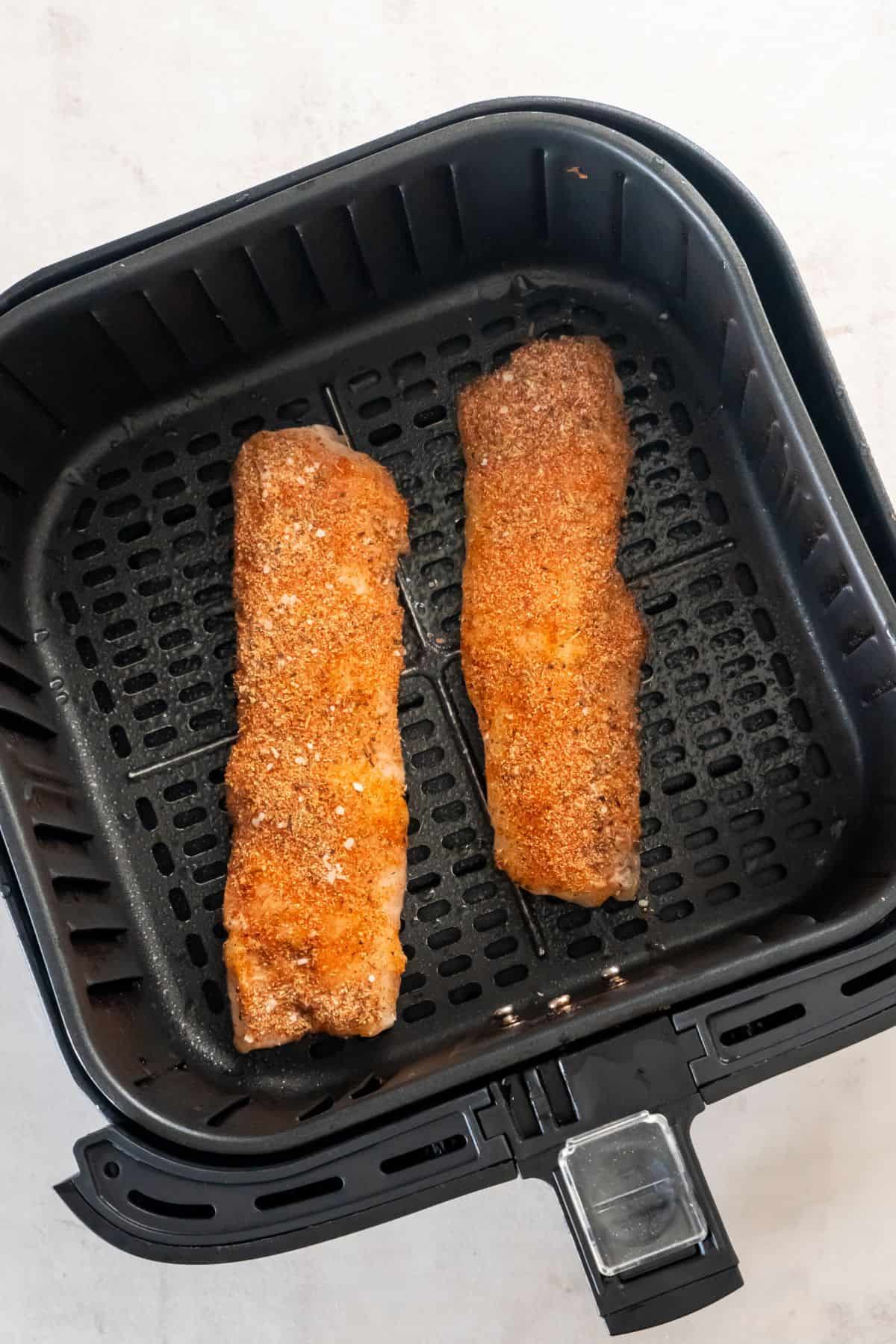 Frozen cod in an air fryer basket about to be air fried.