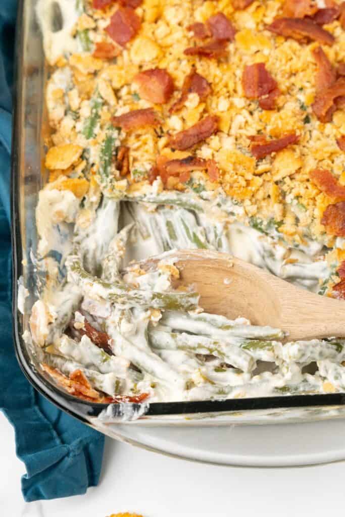 Close up of the green bean casserole in a casserole dish with a wooden spoon in it.
