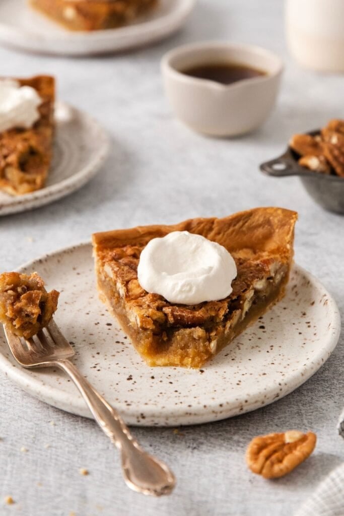 Homemade pecan pie slice on a plate with a bite removed and on the fork next to it.