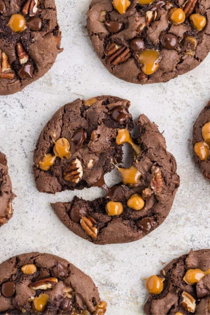 Close up of the turtle cookie recipe with the middle one split in half so you can see the melted chocolate chips and caramel bits stretching.