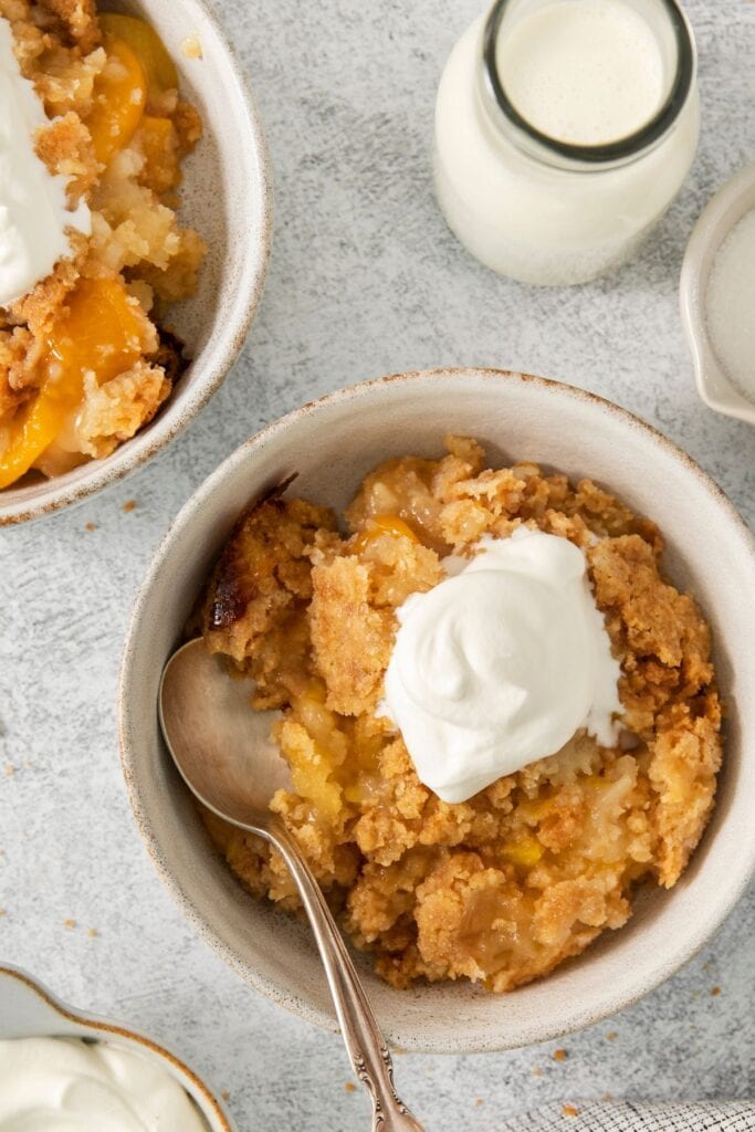 Bowl of peach cobbler with a spoon and whipped cream in it.