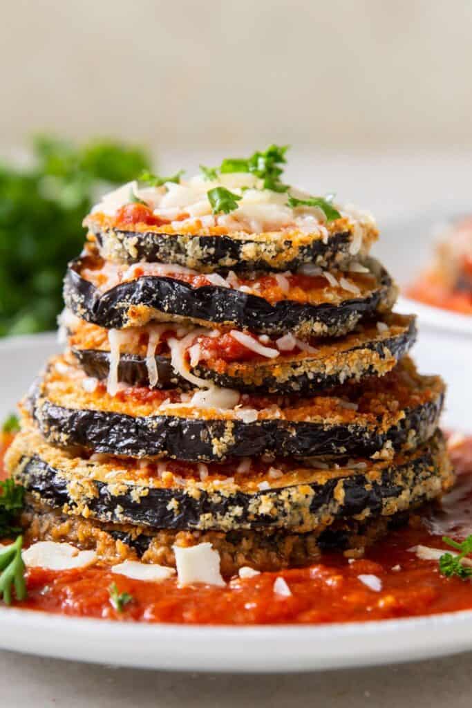 Stacked air fryer eggplant Parmesan on a plate with each slice stacked on top of each other on top of marinara sauce.