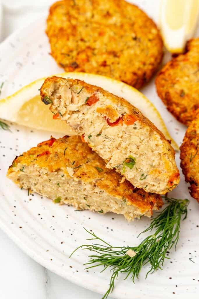 Closeup view of a salmon patty sliced in half on a speckled plate with lemon wedges.